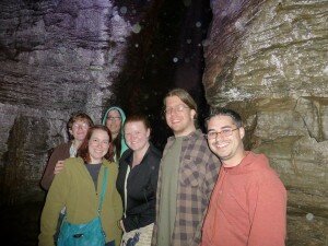 Six people standing in a cave in front of a waterfall. The waterfall is not actually visible.
